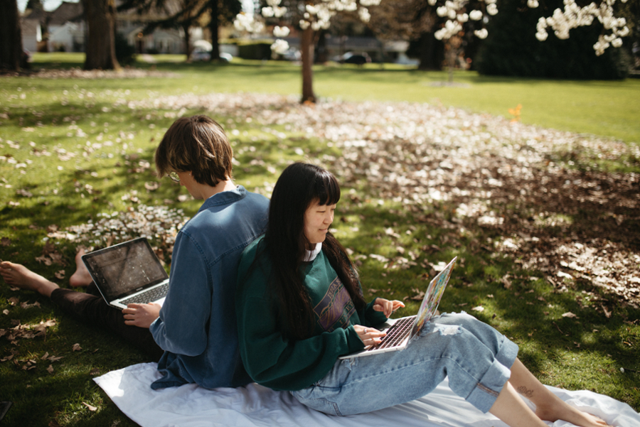 Two students sitting back to back on the Great Lawn working on their computers.